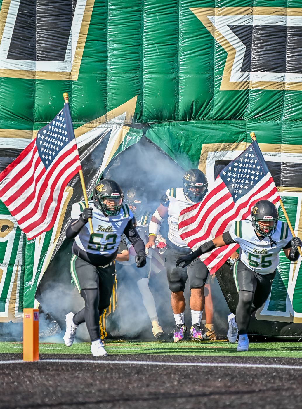 High school football players running onto the field carrying American flags before a game
